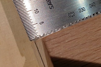 The teeth of a fret slotting saw sticking out between the two pieces of wood I use as depth stops; a string action gauge shows how far the teeth project, roughly 1 mm